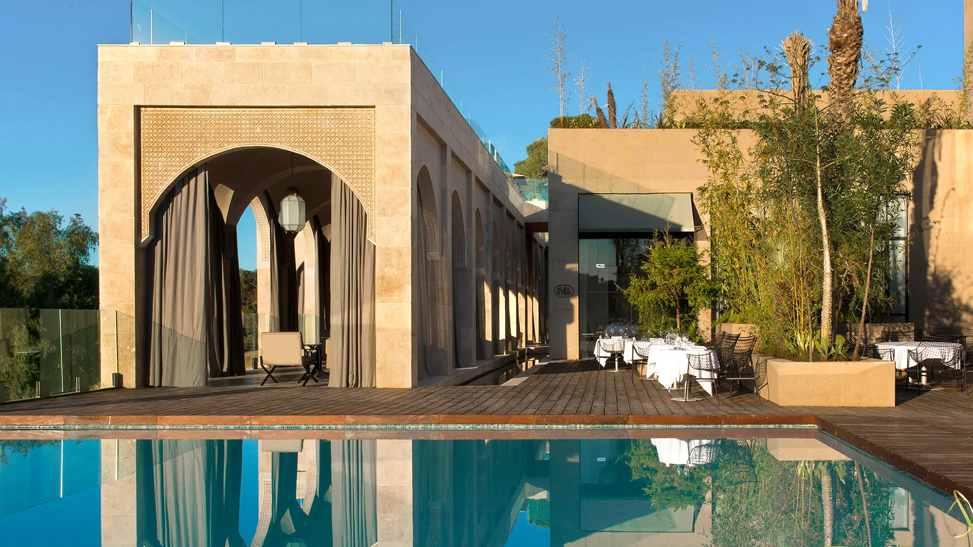 Sandstone terraces stepping down toward a long pool above a Moroccan city